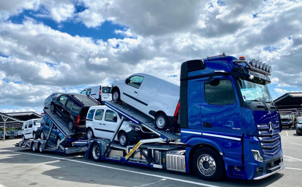 Car Shipping Services truck loaded with multiple vans and cars on a multi-level carrier parked under a cloudy sky.