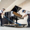 Affordable Piano Moving professionals carefully transporting a grand piano on a dolly outside a modern building