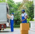 Two movers loading cardboard boxes into a truck outside a house, showcasing Best Moving Services.