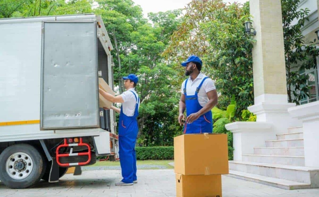 Two movers loading cardboard boxes into a truck outside a house, showcasing Best Moving Services.