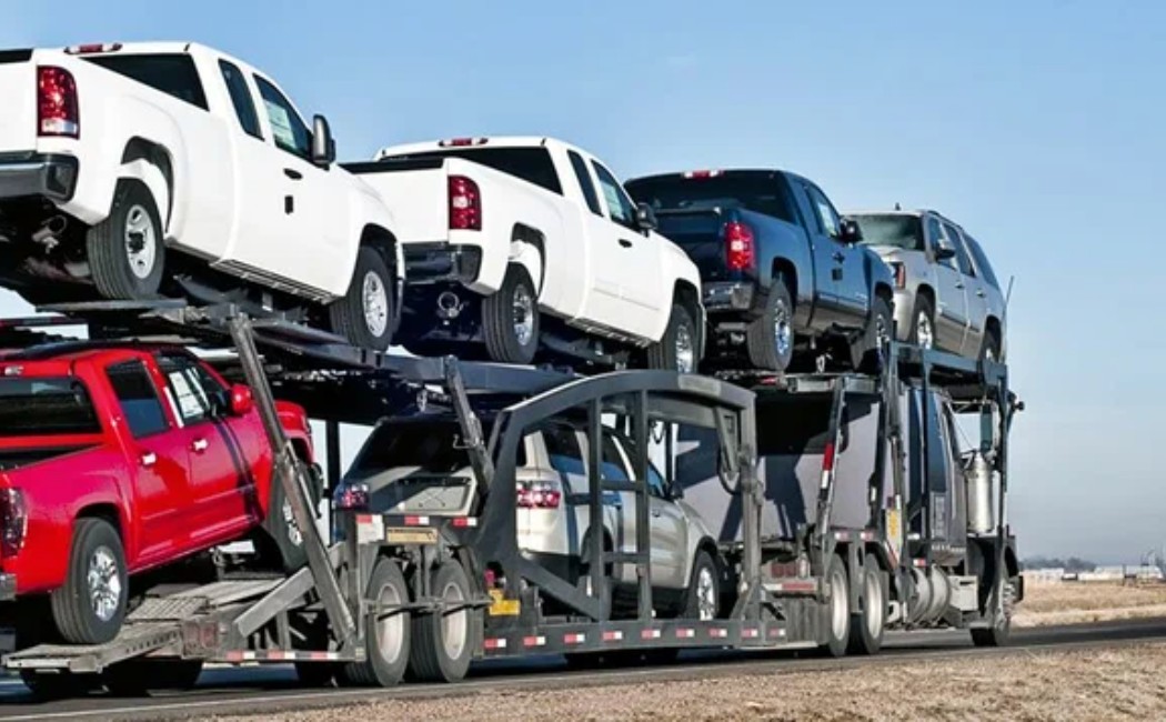 Multi-level auto transport truck carrying several pickup trucks on a highway, representing Car Shipping Services.