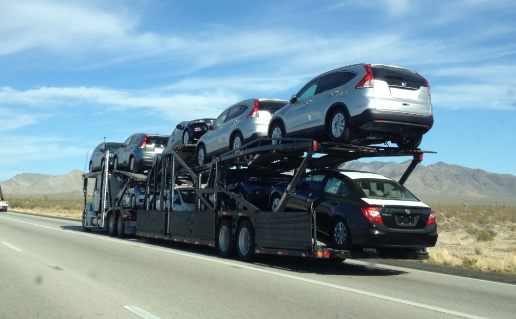 Auto Transportation Services carrier hauling multiple cars on a double-deck trailer across an open desert highway under a clear blue sky.