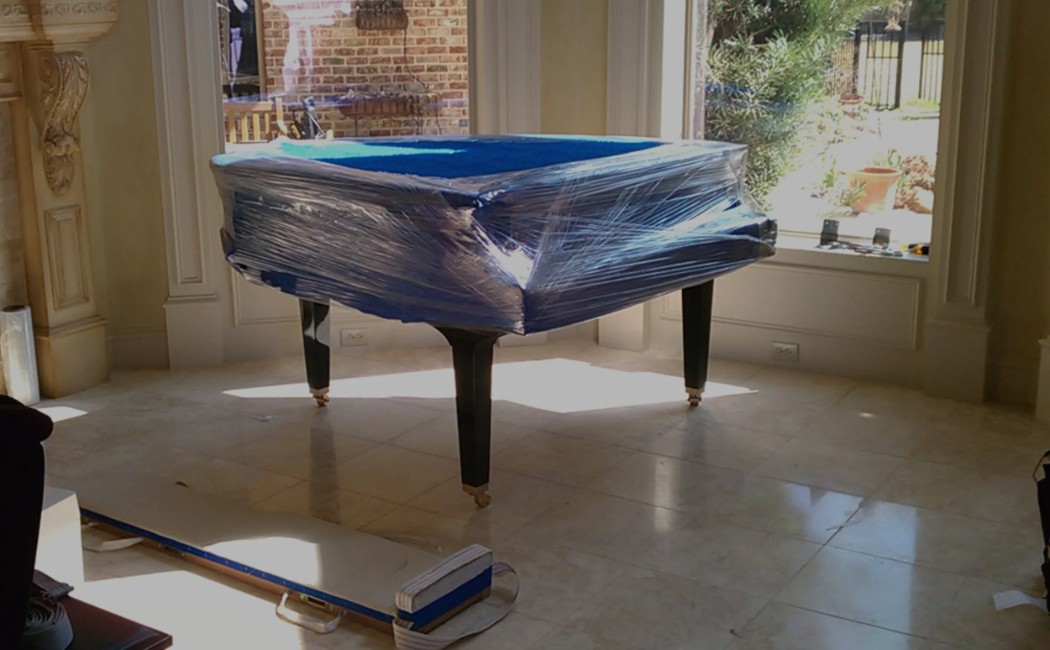 Grand piano wrapped in protective plastic positioned inside a home during a professional piano moving process.