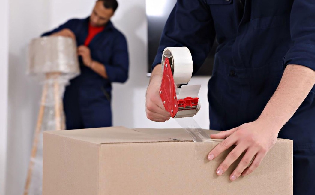 Mover sealing a cardboard box with tape while packing household items for professional Packing Services.