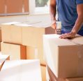 Person sealing cardboard boxes with tape in a home setting for professional Packing Services.