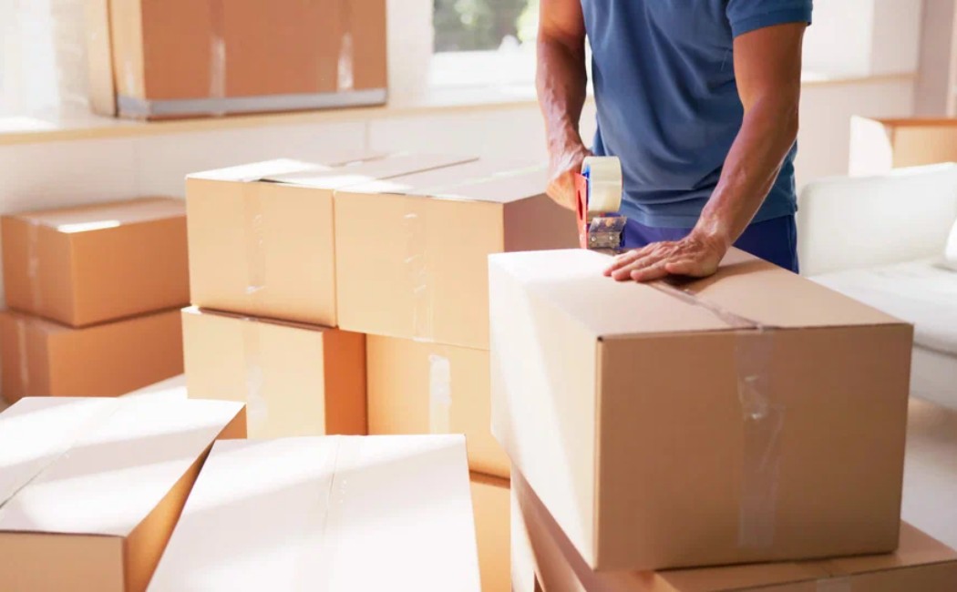 Person sealing cardboard boxes with tape in a home setting for professional Packing Services.